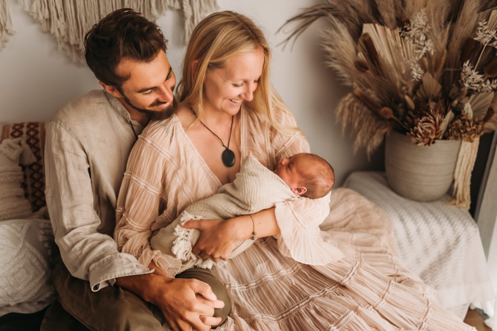 parents smiling and sitting and looking at newborn baby