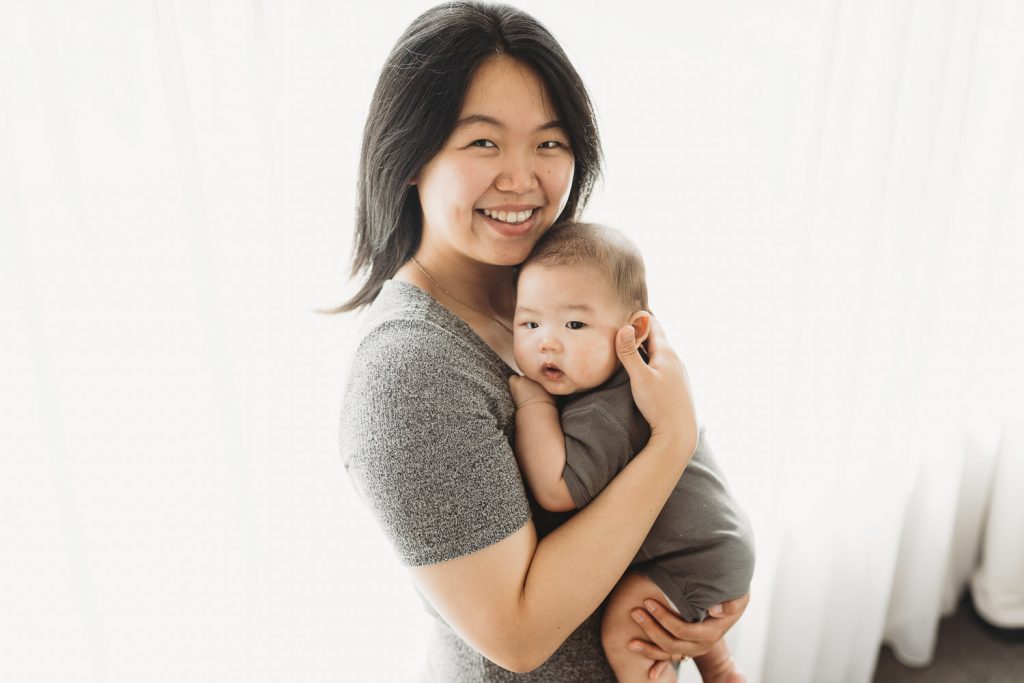mother holding newborn and looking in camera - Auckland Lifestyle Newborn Photographer Amber Farooq
