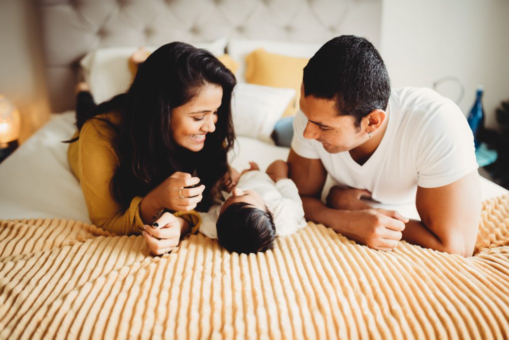 mother father playing with newborn on bed - Auckland Lifestyle Newborn Photographer Amber Farooq