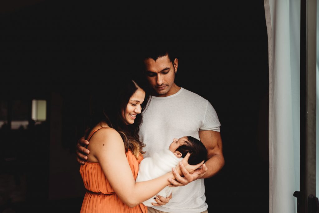 mother father holding newborn and standing on the doorway - Auckland Lifestyle Newborn Photographer Amber Farooq