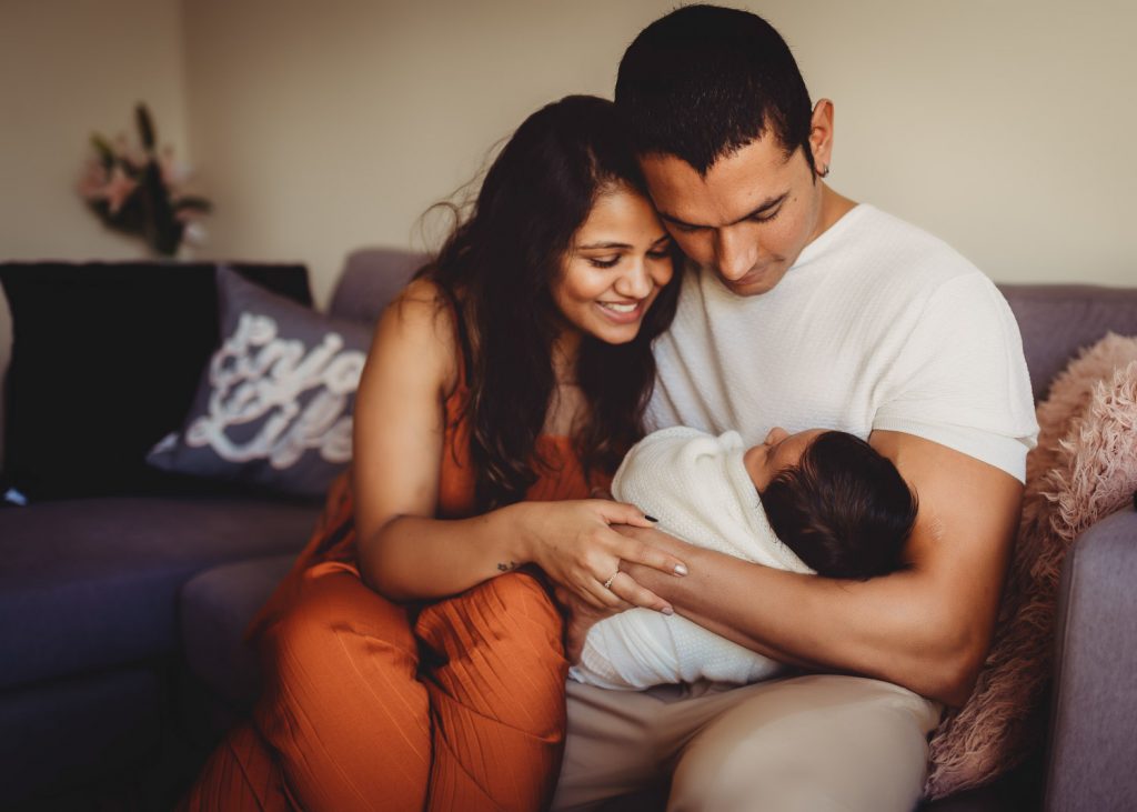 mother father holding newborn sitting on sofa - Auckland Lifestyle Newborn Photographer Amber Farooq