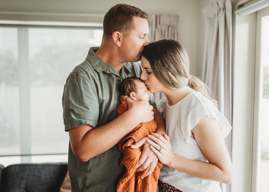 father kissing mother and mother kissing newborn