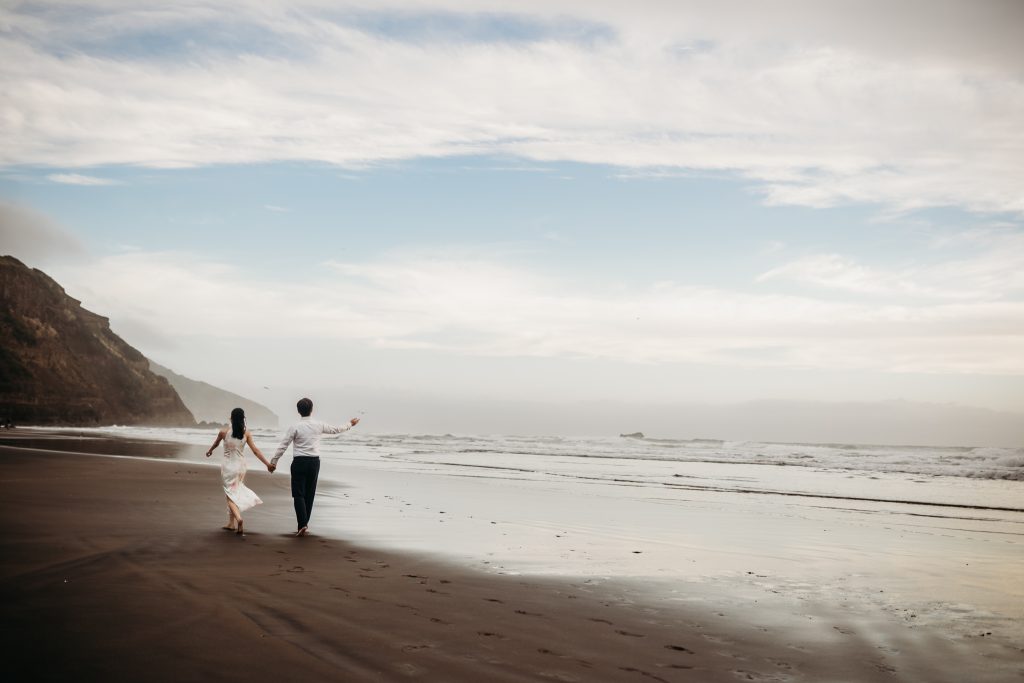 Soft sand and crashing waves create a natural backdrop for Lishan and Ernest's honeymoon portraits at Muriwai Beach.