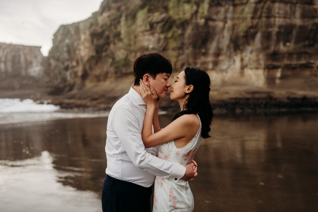 Lishan playfully throws sand at Ernest during their romantic photoshoot at Muriwai Beach, adding a touch of lightheartedness.