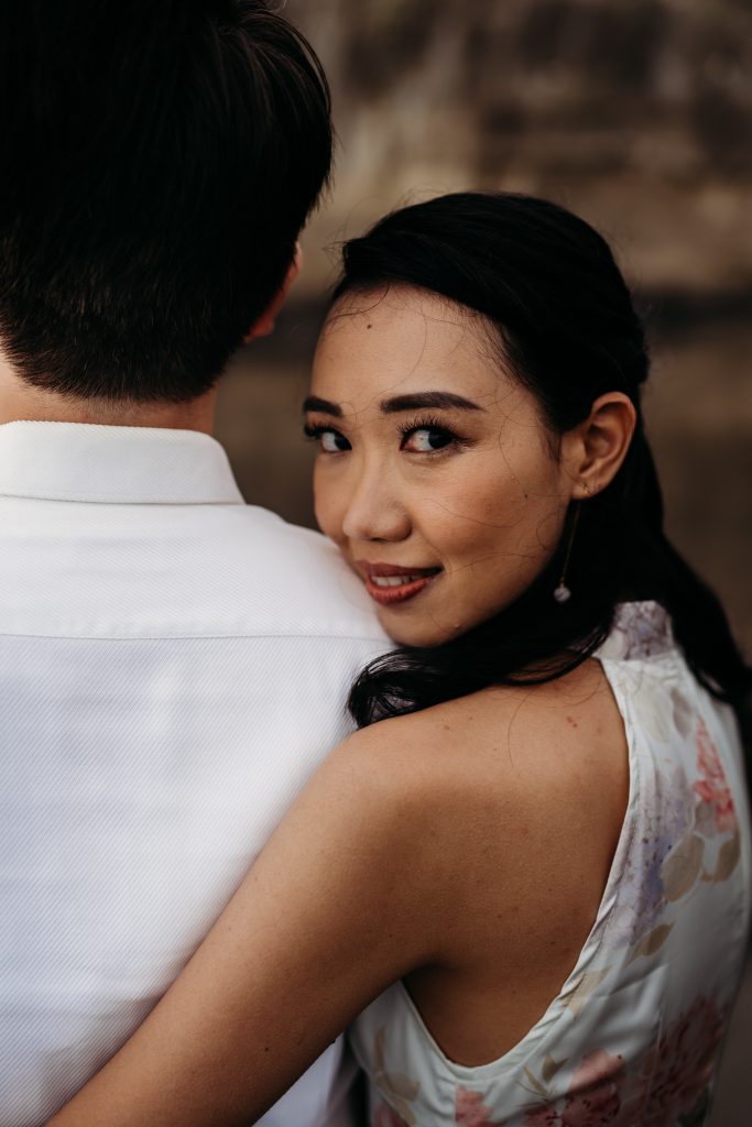 Lishan and Ernest twirl on the beach, their laughter echoing amidst the beauty of Muriwai Beach on their honeymoon.