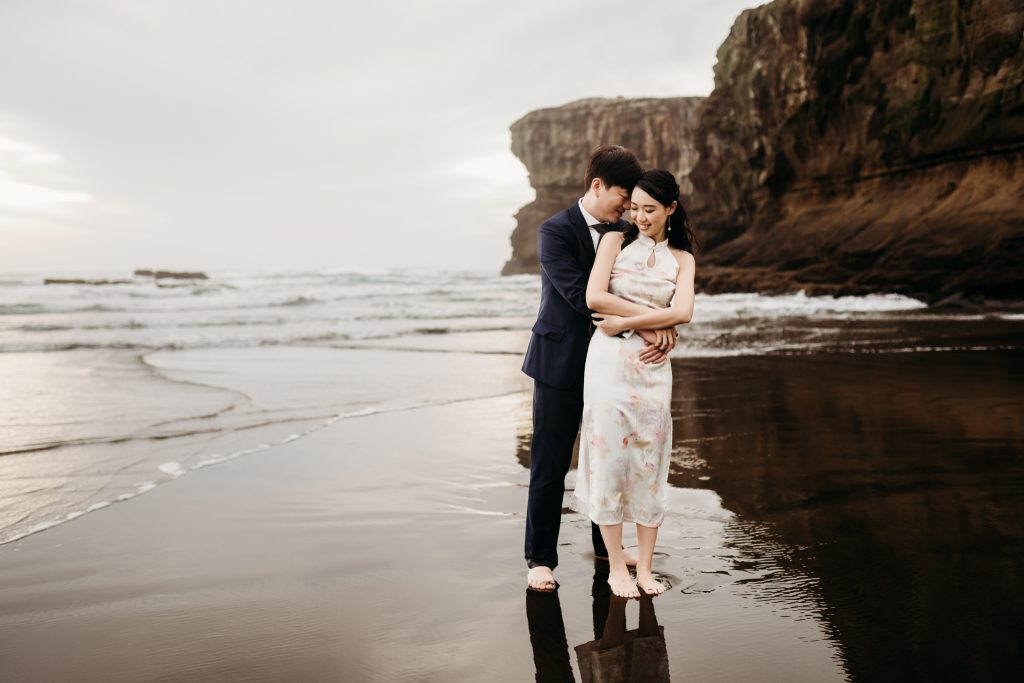 Lishan and Ernest embrace the rugged beauty of Muriwai Beach on their honeymoon adventure in Auckland.