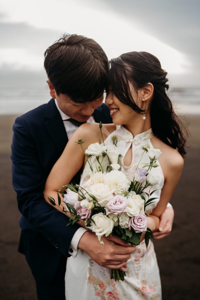 Golden light and endless love: The setting sun bathes Lishan and Ernest in a warm glow during their Muriwai Beach honeymoon shoot.