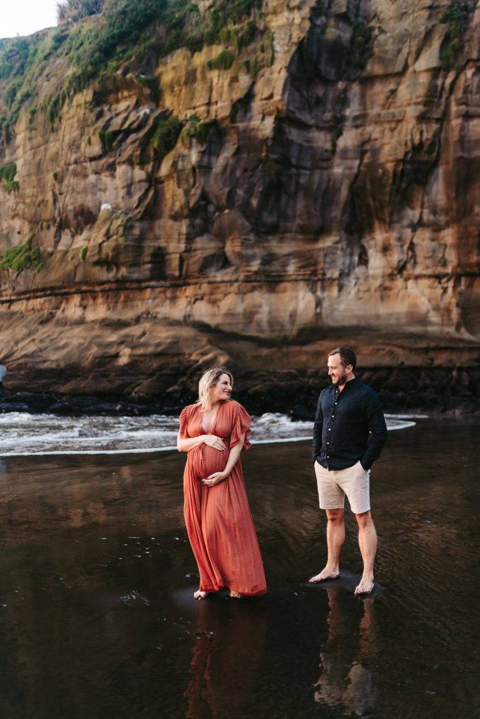 Auckland maternity photo shoot: Expecting mother basks in the golden light of sunrise on a peaceful Auckland beach.