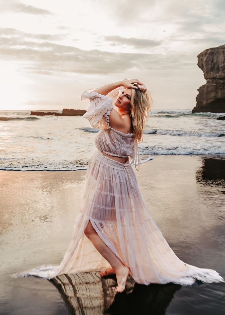 Auckland maternity photography studio: Mom-to-be dressed in a flowing gown, showcasing her baby bump in a studio setting.