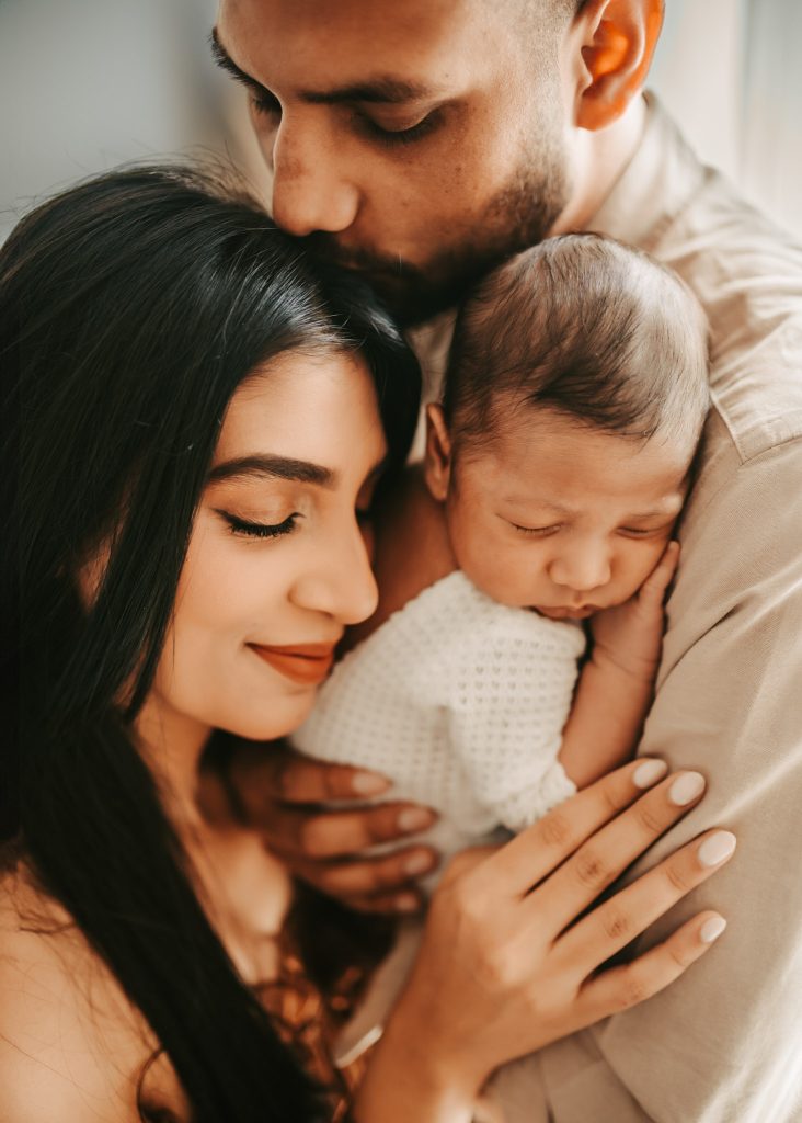 Auckland newborn photography studio: A lifestyle session filled with tenderness as Arham's parents embrace him.