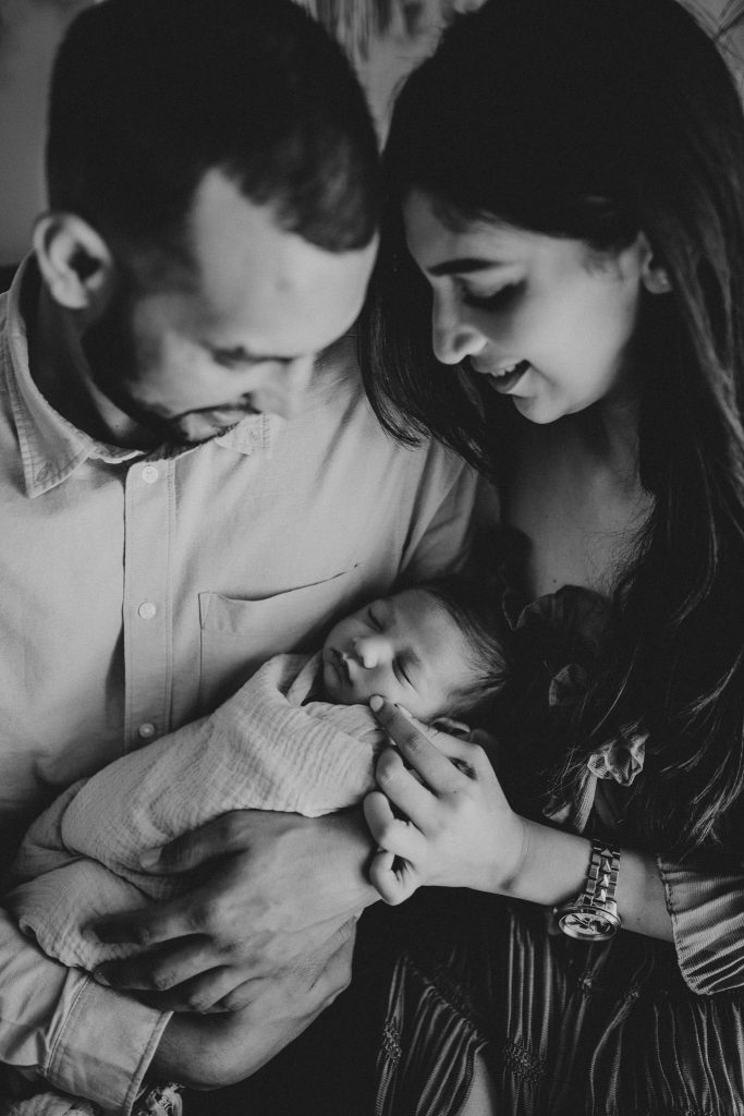 Newborn lifestyle session in Auckland: Soft light illuminates Arham and his parents, creating a timeless portrait of love.