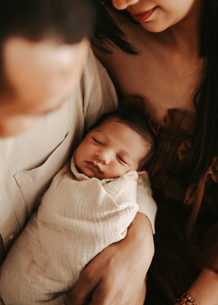 Auckland newborn photography: Proud parents cuddle their baby boy Arham in a heartwarming lifestyle session.