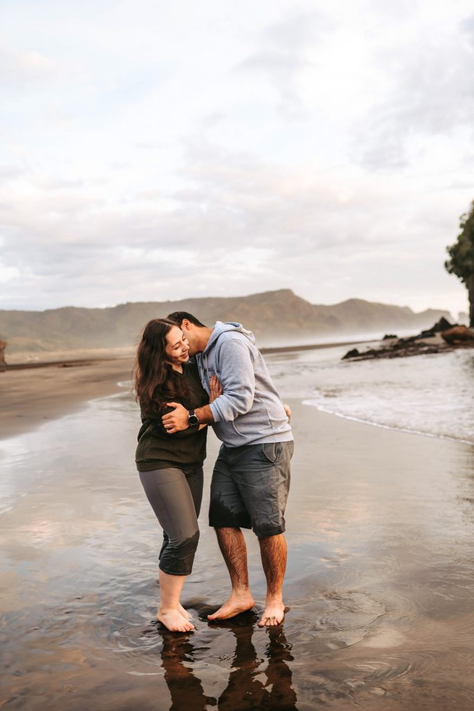 Bethells Beach anniversary portraits: Mas playfully carries Huda amidst the black sand dunes, celebrating their love with a touch of fun.